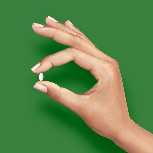 A manicured hand holds a small white up&up Cetirizine Hydrochloride Allergy Relief Tablet (2 Pack, 300 Count Each), promising 24-hour relief against a solid green background.