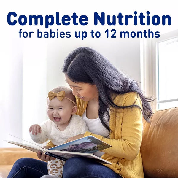 A woman in a yellow sweater reads to her smiling baby in a bow headband. Text: Enfamil 2 Pack Milk-Based Powder Infant Formula 0-12 Months offers immune support, brain-building DHA, and essential nutrients for infants.