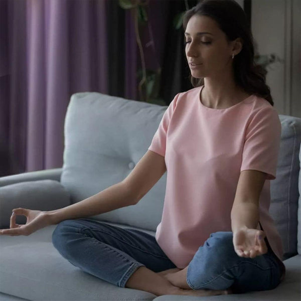 A woman meditates peacefully on a sofa, embracing inner calm with the antioxidant action of Vicks 2 Pack - ZzzQuil Pure Zzzs Triple Action Gummy Melatonin Sleep Supplement 42ct.