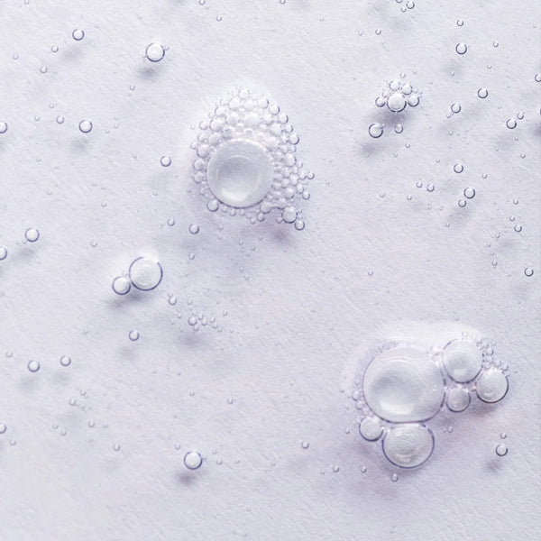 Clear gel-like bubbles of various sizes, featuring Vegan Keratin, are scattered on a white textured surface beside the Raw Sugar Simply Straight Keratin Straightening Serum 4oz (3 Pack) by Raw Sugar.