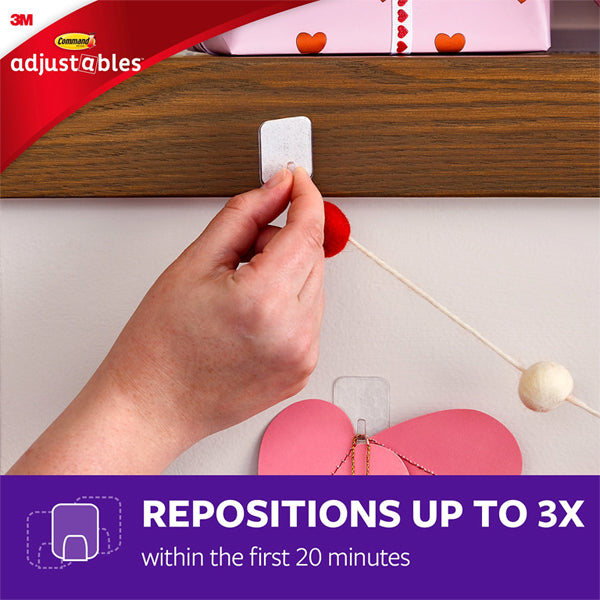 A hand applies a 3M 3 Pack - 17840CLR-14ES Adjustables Clip & Strip to a wooden shelf for damage-free hanging of decorative string. Reposition up to 3X within the first 20 minutes—it includes 14 repositionable clips and 30 strips per pack.