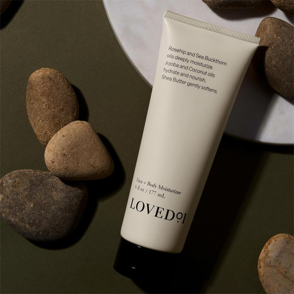 A 3 Pack of Loved 01 Face + Body Moisturizer with Rosehip & Sea Buckthorn (6oz) is displayed on a flat surface, surrounded by smooth stones and a white plate.