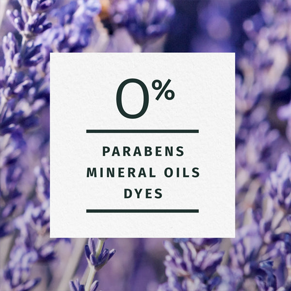 A centered text reading 0% parabens, mineral oils, dyes appears on a white square over blurred purple flowers, highlighting natural ingredients like jojoba oil in the Herbal Essences Jojoba Oil & Lavender Curls Shampoo 3 Pack.