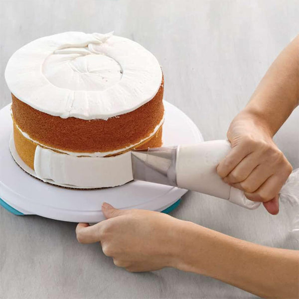 Someone uses a Wilton Disposable 16 Decorating Bag from the 4 Pack (12 Count Each) to apply white frosting to the side of a layered cake, steadying it on a rotating stand.