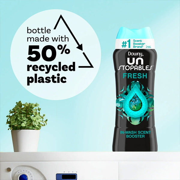 A 5 Pack of Downy Unstopables Laundry Scent Booster Beads Fresh Scent (5.7 oz) is shown beside a plant, featuring text that highlights the bottle is made with 50% recycled plastic—enjoy lasting freshness and care for the environment.