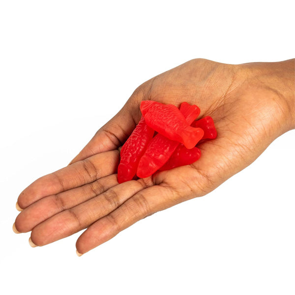 A hand holds several red, fish-shaped Swedish Fish candies from the 6 Pack - Swedish Fish Soft & Chewy Candy 8oz Bags against a white background.