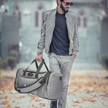 A man in a grey jacket and pants walks outside on a leaf-covered path, carrying the Erozul Legion Smell Proof Duffel Bag with TSA Combination Lock by Erozul.