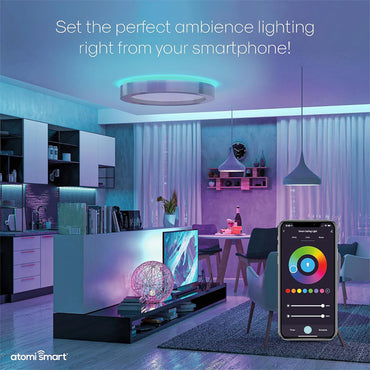 A modern living room and kitchen glow with colorful light from the Atomi Smart WiFi LED Ceiling Light (2200 Lumens, 24W, color changing, dimmable), easily controlled by the Atomi Smart app or by voice with Alexa or Google Assistant.