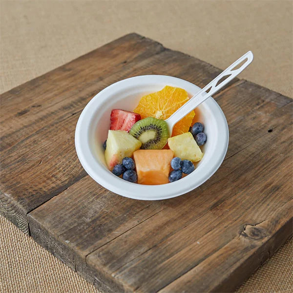 A 12oz Emerald Ecovations Tree-Free Compostable Bowl from the 250 Count pack is filled with assorted fruit and a plastic spoon, placed on a wooden board for an eco-friendly dining option.