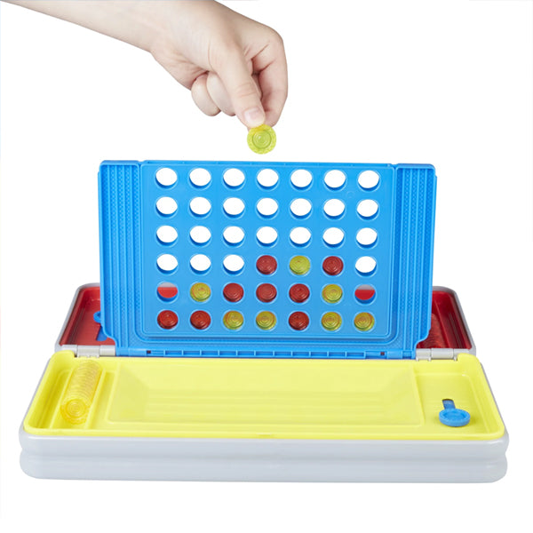A hand holds a yellow piece above the Hasbro Gaming Road Trip Series Connect 4 Board Game in its portable case, with red and yellow discs on the blue board—perfect travel fun from Hasbro.