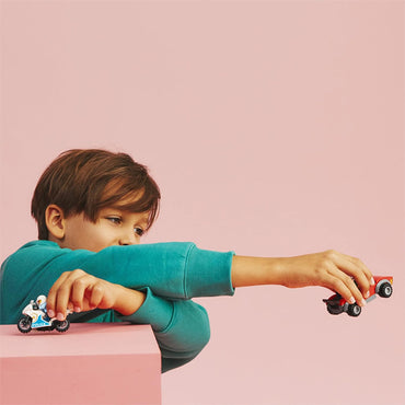 A young boy in a teal sweatshirt holds the LEGO City Police Bike Car Chase Racing Vehicle & Motorbike 60392 by LEGO, ready for high-speed crook-catching fun, against a plain pink background.