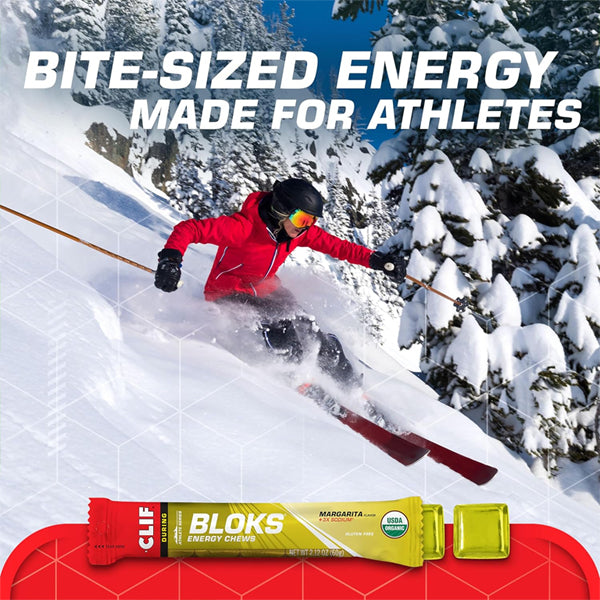 A skier in a red jacket speeds down a snowy slope above a Clif BLOKS Energy Chews Margarita Flavor with 3X Sodium pack, featuring the text “Bite-sized fast fuel made for athletes.”.