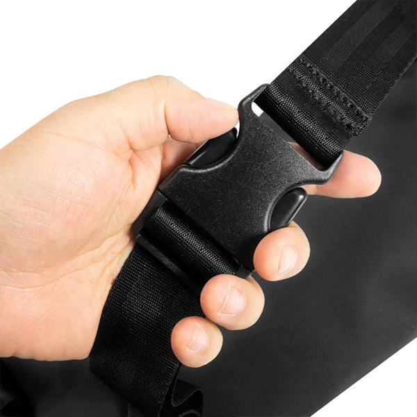 A hand holds a black plastic side-release buckle on a strap, part of the Skunk Drifter Medium Crossbody Bag in Metal Gray, featuring 100% smell and weather proof carbon lining by Skunk.