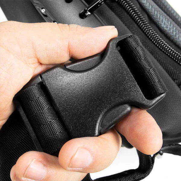 A hand holds a black plastic side-release buckle on a strap, with part of a Skunk Drifter Small Crossbody Bag (100% smell & weather proof carbon lining, Metal Gray) by Skunk visible in the background.