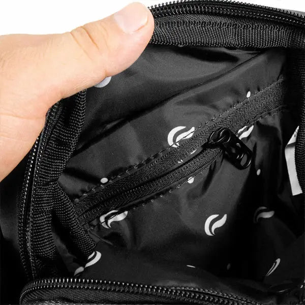 A hand opens the Skunk Drifter Small Crossbody Bag in Metal Gray, showing its white-patterned interior and zip pocket—this bag is 100% smell and weather proof with carbon lining featuring SK9® Smell Proof Tech.