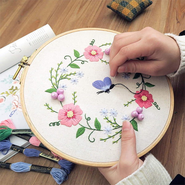 Someone is embroidering a floral and butterfly design on fabric using the YITOHOP Embroidery Cross Stitch Kit, which includes 5 bamboo hoops, 100 color threads, 3 pieces of Aida cloth, and more.