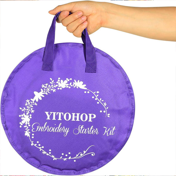 A hand holds a round, purple YITOHOP bag labeled Embroidery Cross Stitch Kit with a floral design—ideal for organizing the kit’s 5 bamboo hoops, 100 color threads, Aida cloth, and more.