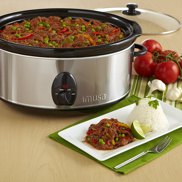 The IMUSA Electric Stainless Steel PTFE Nonstick Slow Cooker 3.7 Quarts is filled with shredded beef and veggies, behind a plate of shredded beef, rice, and lime on a table with tomatoes, garlic, and cilantro for an easy one-pot meal.