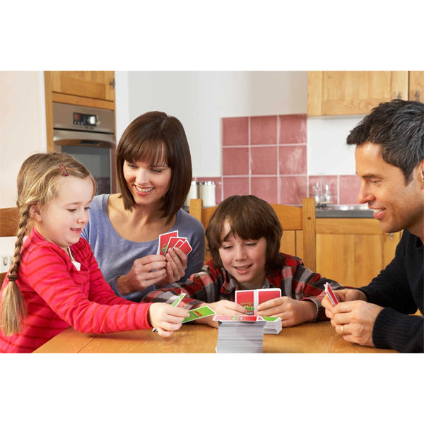 A family of four enjoys quality time at a wooden kitchen table, smiling and playing Mattel Games Apples to Apples Junior the Game of Crazy Comparisons! by Mattel—expanding their vocabulary while having fun together.