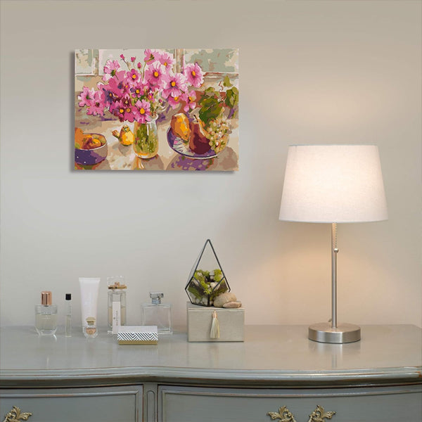 A table with a lamp and small decor sits beneath a Ledgebay Paint by Number for Adults Framed Canvas—Cosmos from The Garden, 12 x 16, hanging on the wall.