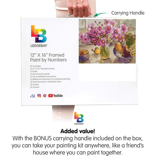 A person holds a Ledgebay Paint by Number for Adults Framed Canvas - Cosmos from The Garden (12 x 16) box by its handle; this arts and crafts kit displays the licensed flower artwork on the front.