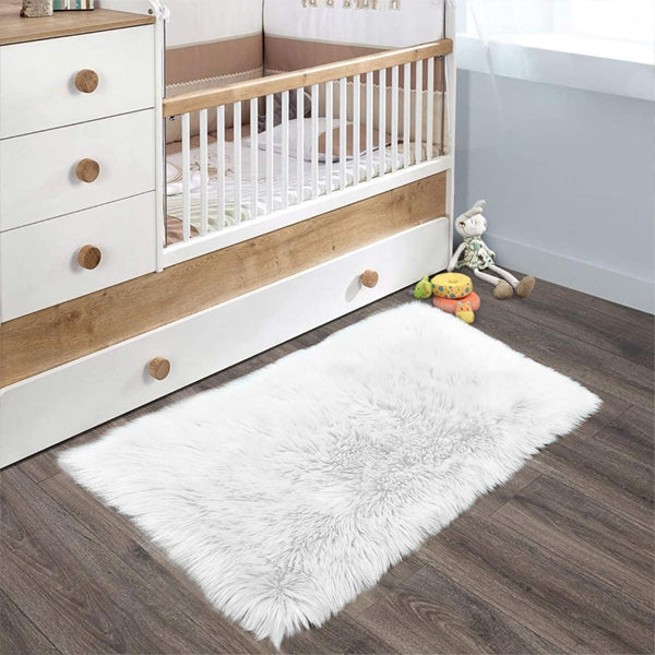 The Latepis White Luxury Faux Fur Sheepskin Rug 2x3 adds a plush, cozy touch to the nursery’s dark wood floor in front of the crib and dresser, with toys and a stuffed animal completing the inviting space.