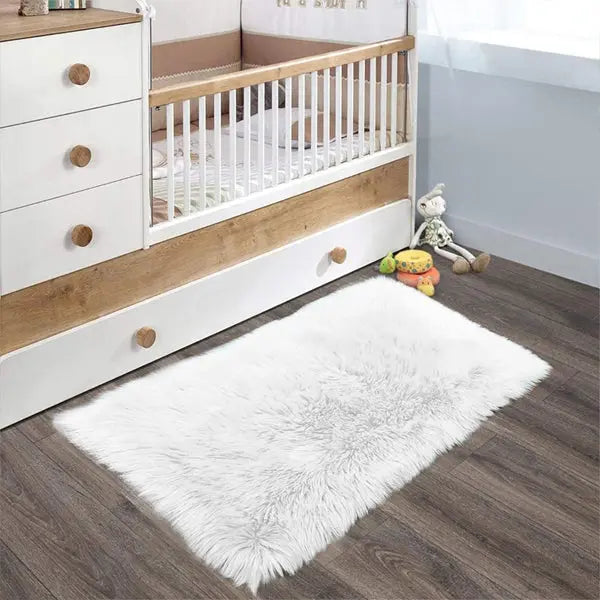 The Latepis White Luxury Faux Fur Sheepskin Rug 2x3 adds a plush, cozy touch to the nursery’s dark wood floor in front of the crib and dresser, with toys and a stuffed animal completing the inviting space.