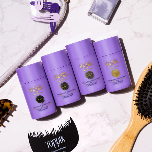 Four Toppik Hair Fiber Powder Hair Thickener for Women Medium Brown 12g bottles are arranged on a flat surface with a hairbrush, hair clips, a zipper pouch, and a nail polish bottle.