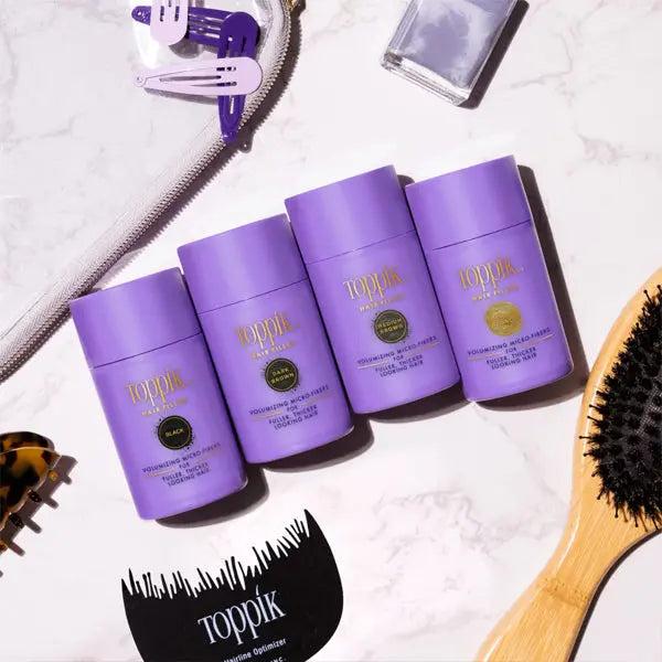 Four Toppik Hair Fiber Powder Hair Thickener for Women Medium Brown 12g bottles are arranged on a flat surface with a hairbrush, hair clips, a zipper pouch, and a nail polish bottle.