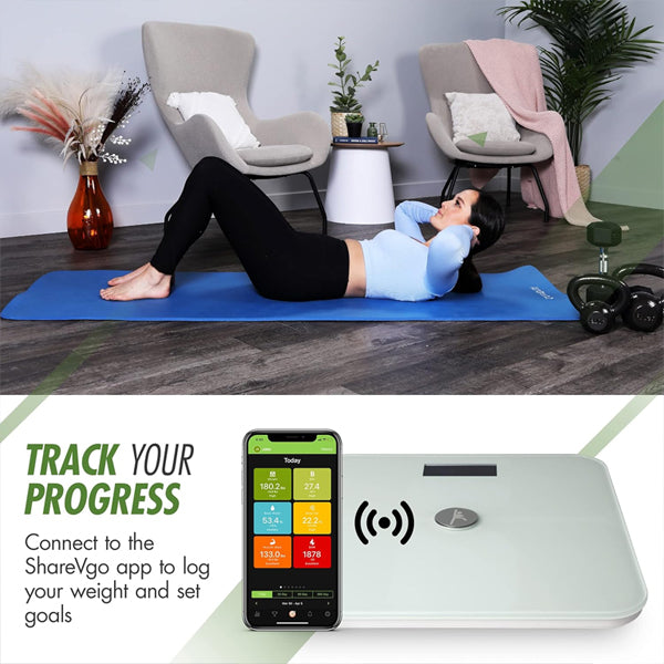 A woman does crunches on a blue mat in a living room; nearby, a ShareVgo Smart Digital Body Weight Scale SWS200 – White and a mobile screen show progress tracking with the ShareVgo app.