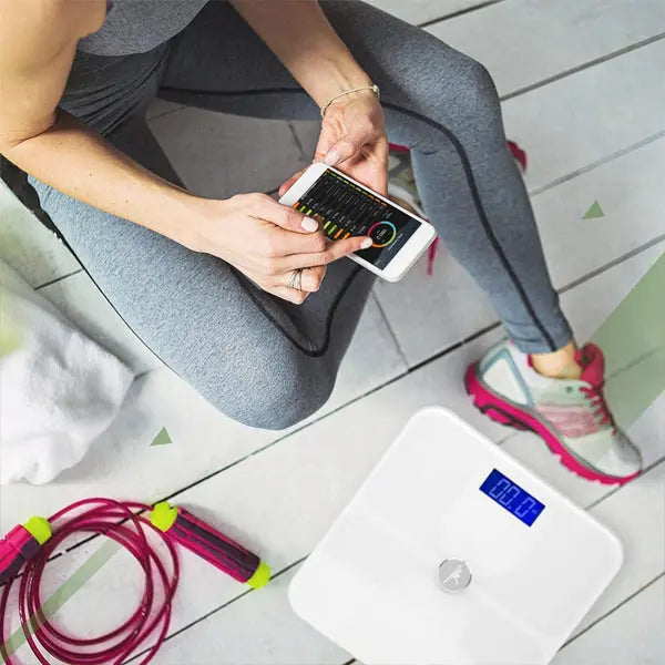 Wearing athletic wear, a person sits on the floor holding a smartphone near the ShareVgo Smart Digital Body Weight Scale SWS200 (White) and a jump rope, highlighting fitness and health tracking with ShareVgo products.