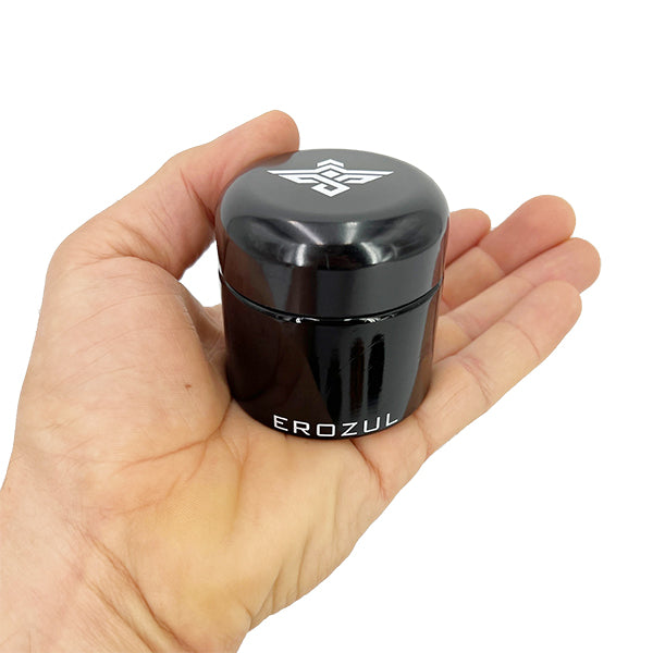A hand holds an Erozul 60ml Screw Top Wide Mouth Glass UV Jar from a 3 pack, featuring the Erozul brand and airtight, smell proof storage—ideal for preserving freshness with its premium black design and white geometric logo on the lid.