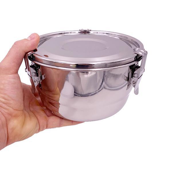 A hand holds the CVault 2 Liter Humidity Control Airtight Metal Stash Smell Proof Container by CVault, featuring a locking lid and side clasps for humidity curing, against a white background.