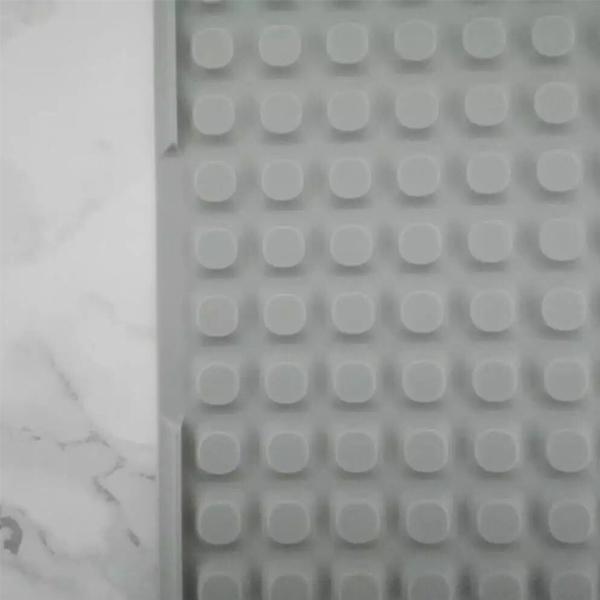 A gray Deal Society Self Draining Silicone Dish Drying Mat (16 x 12, Twin Pack) with raised bumps is placed on a white marble surface.