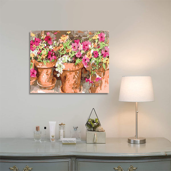 A wall features the Ledgebay Paint by Numbers Kit for Adults - Sweet Petunias 16 x 20 framed painting above a dresser holding a lamp, toiletries, and small decor.