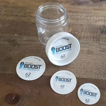 An open glass jar with four Integra Boost Humidity Cap Pack 51mm 62% by Integra Boost sits on a wooden surface, ensuring optimal humidity control.